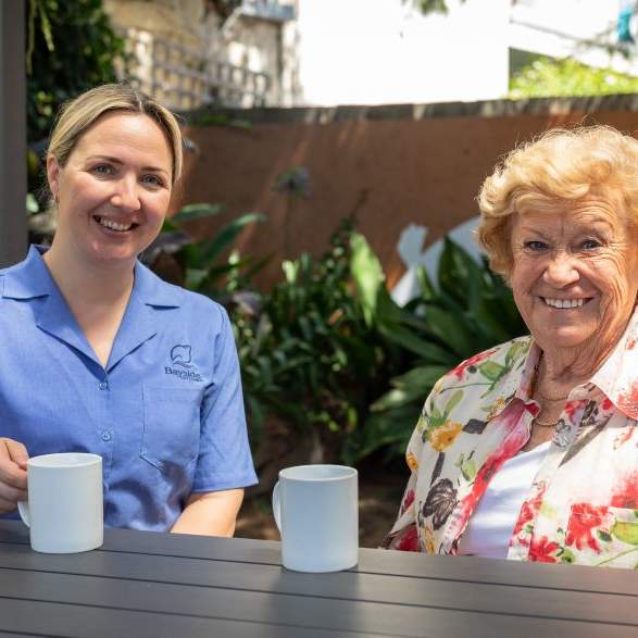 An female aged care worker sitting having a cup of tea with an older female client