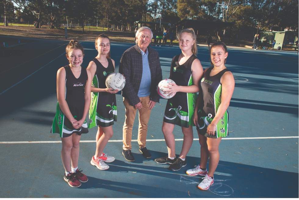 Four teenage girls in netball uniform standing with a local Councilor at courts