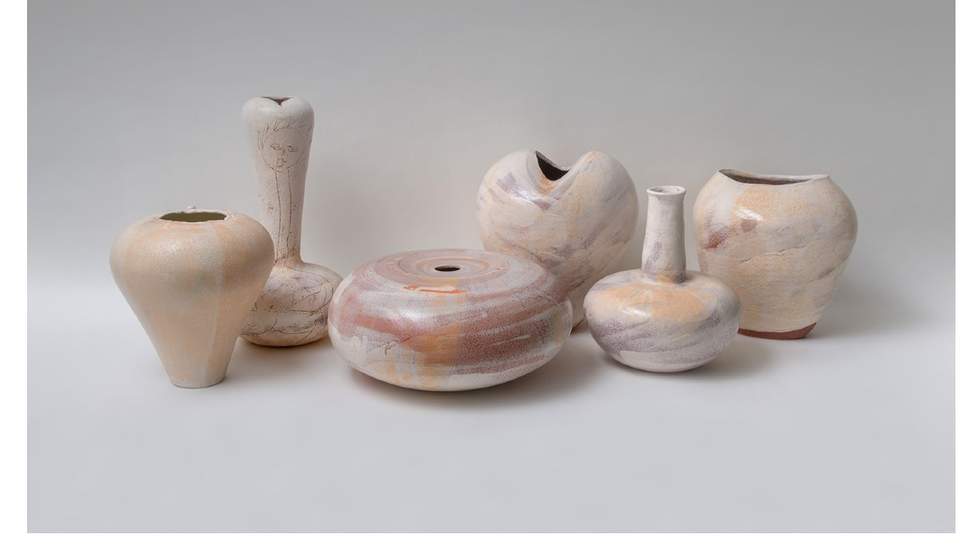 Ceramic vessels of different size and form painted in a white wash glaze, grouped together against a plain background. 