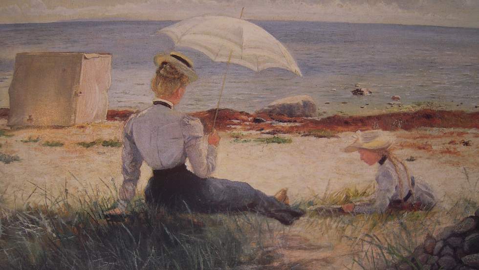 Painting of a woman and child dressed in late 1800s attire, sit on the sand looking towards the sea. The woman holds a white parasol while the girl leisurely lies beside her