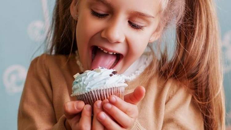 Little girl licking cup cake.