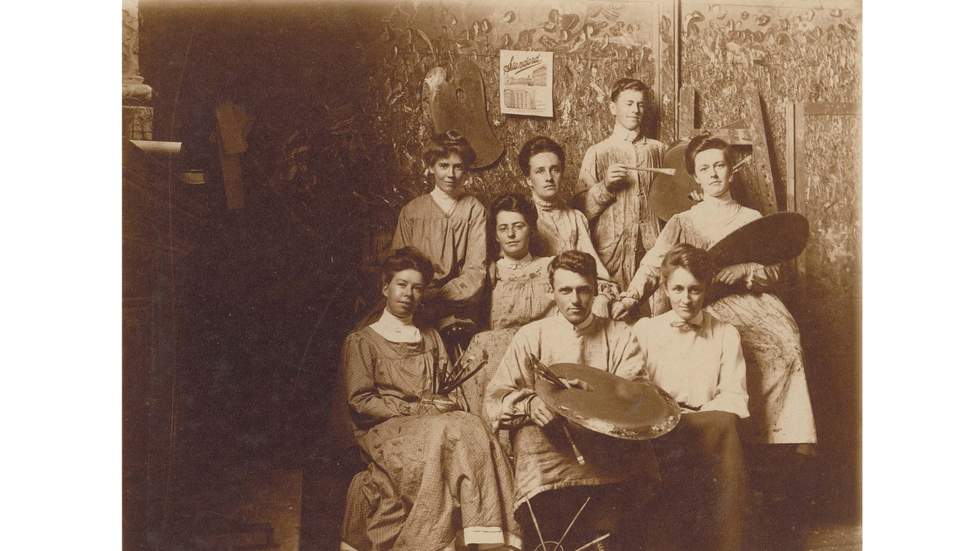 Black and white photo of men and women students seated and standing wearing smocks.