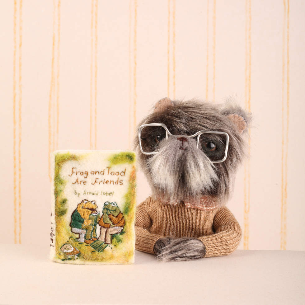 Bear wearing glasses sat next to book titled 'Frog and Toad are Friends'.