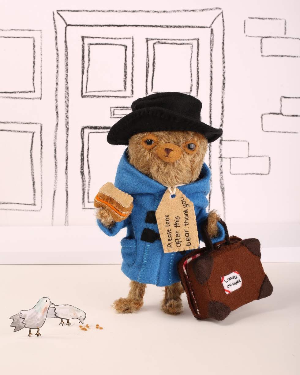 A three dimensional bear dressed as Paddington Bear holding a suitcase.