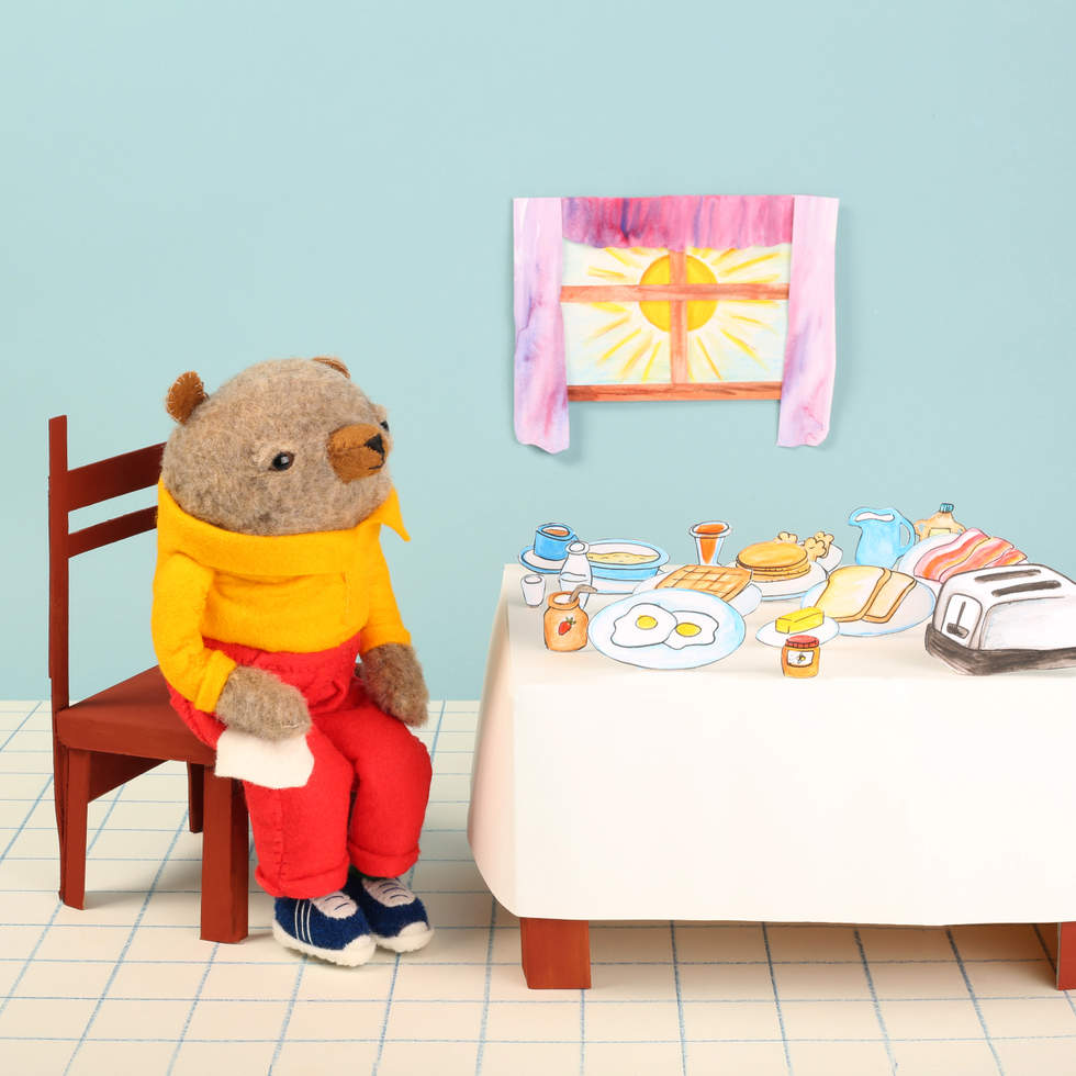 A three dimensional scene of a bear seated at a table with breakfast food.