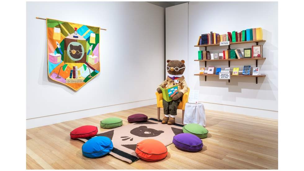 An interior view of an exhibition with a large seated bear holding a book.