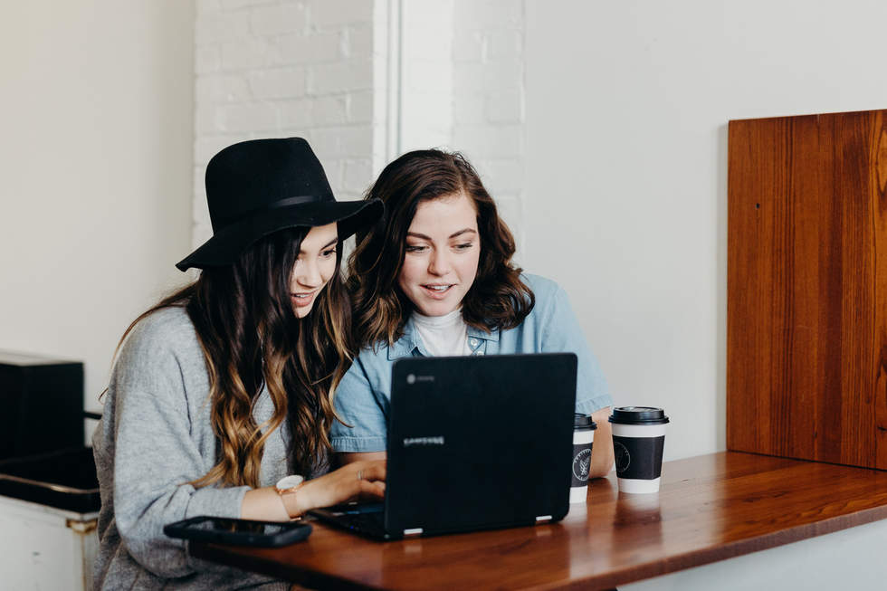 Two young women looking at laptop, with coffee cups
