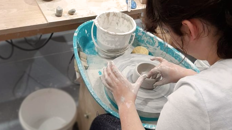 Young person using a pottery wheel to make a bowl