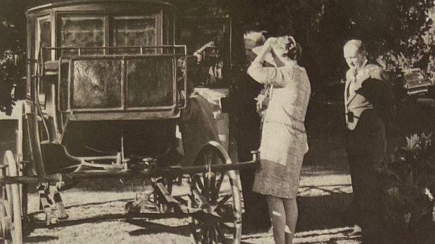 Black and white photo of three adults standing beside an old carriage