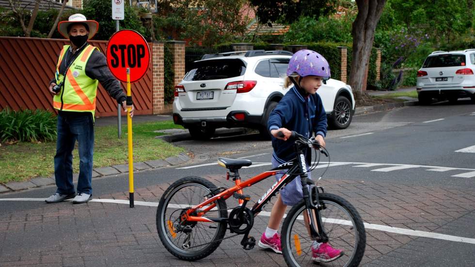 Crossing supervisor in hi-vis vest with STOP sign as child crosses the road pushing her bike