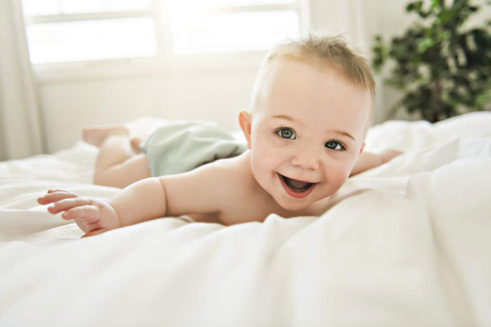 Baby in reusable nappy lying on a bed smiling