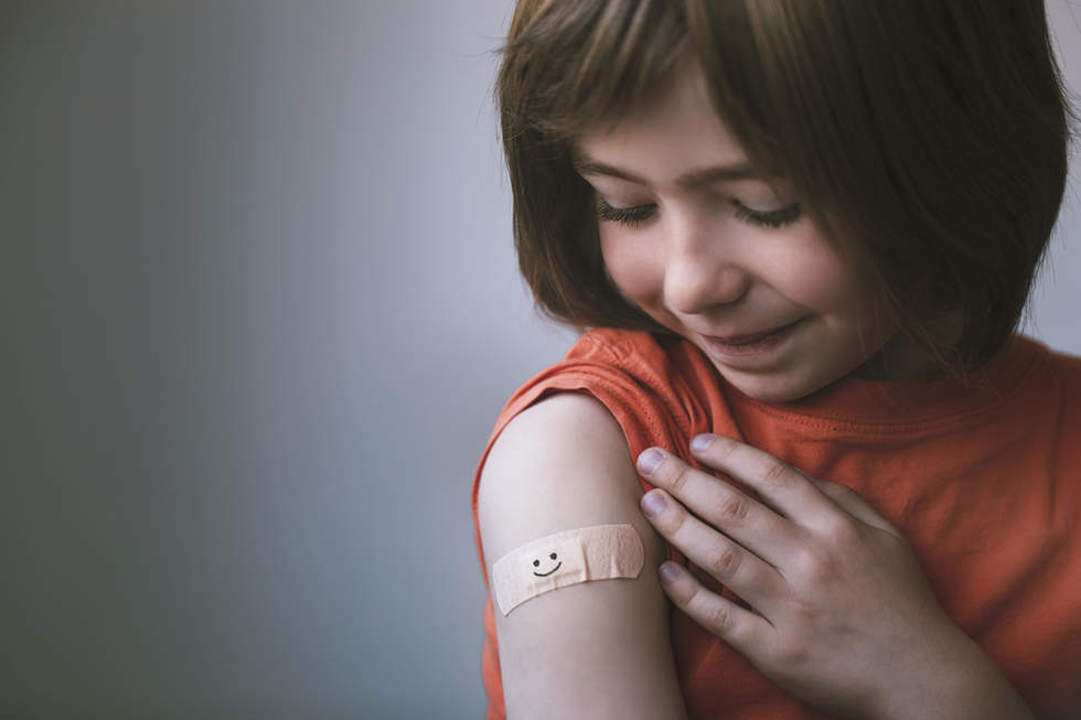Smiling young girl looks at the bandaid on her upper arm