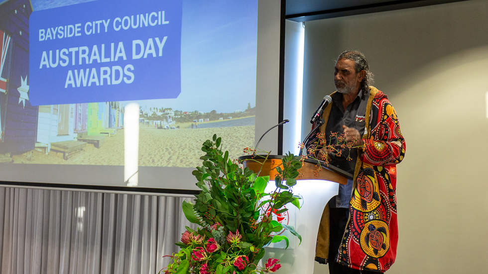Man talking to crowd at Australia Day Awards wearing bright indigenous coat
