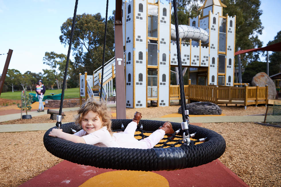 Young girl on a swing in front of a playground castle