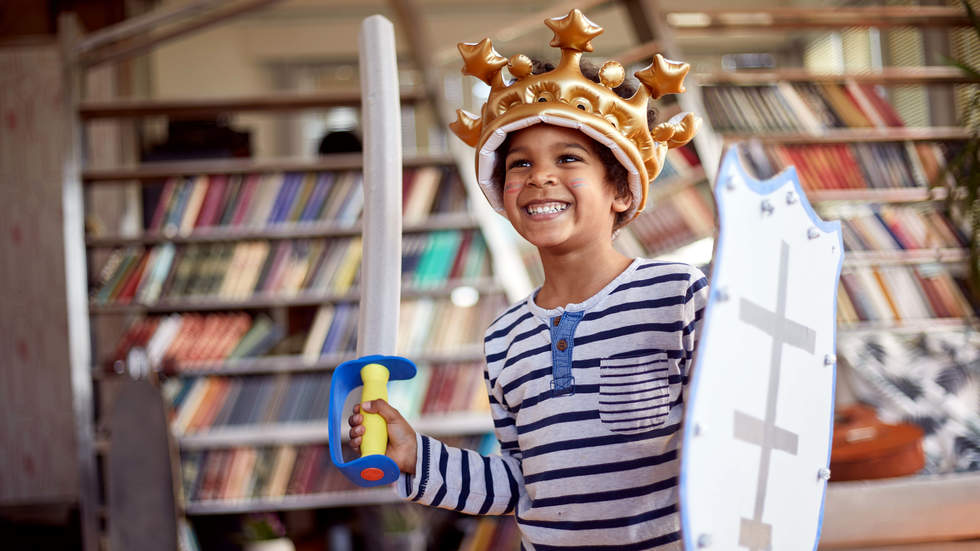 Little boy dressed as knight in front of bookshelves