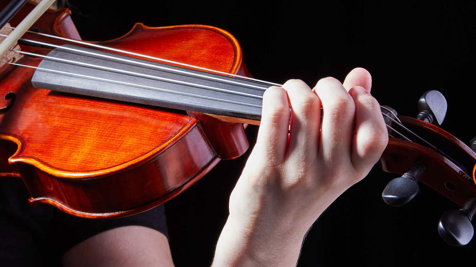 Close up view of someone playing the violin. The colour of the violin is vibrant against a black background.