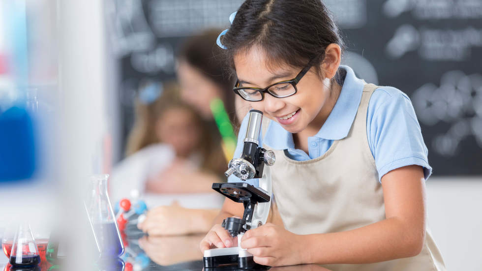 Little girl smiling and looking into a microscope