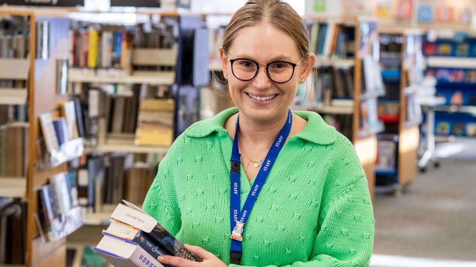 Librarian standing in the library smiling and holding books