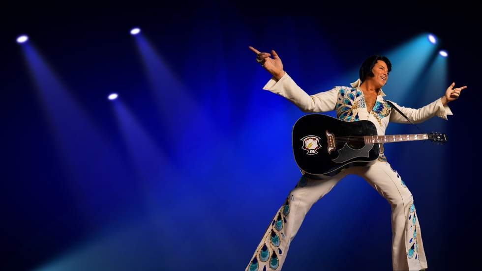 A man dressed as Elvis on stage with a guitar. 