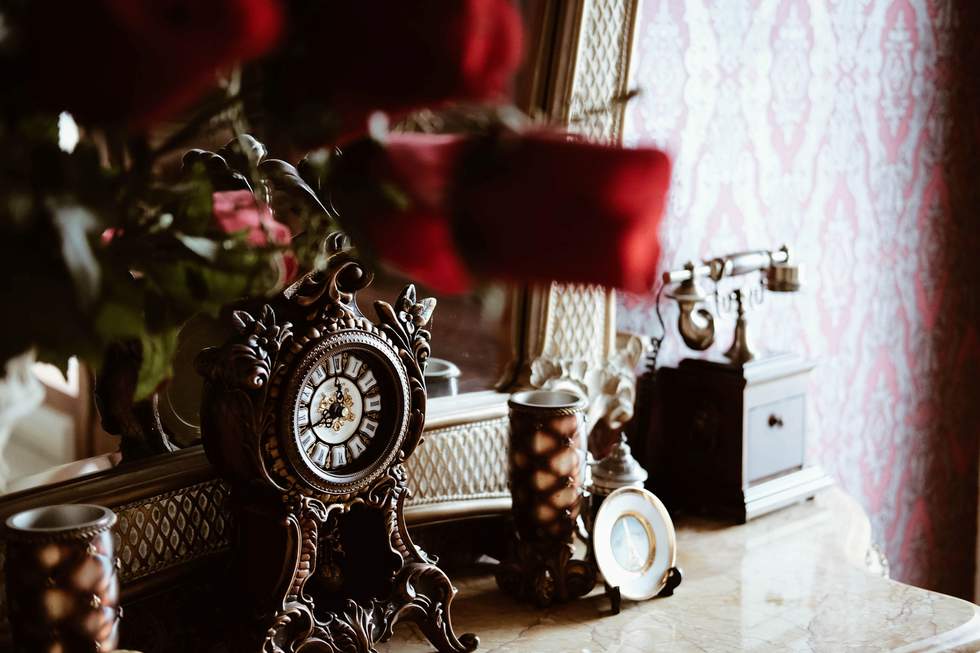 Antique clock on a dresser with flowers in background. 