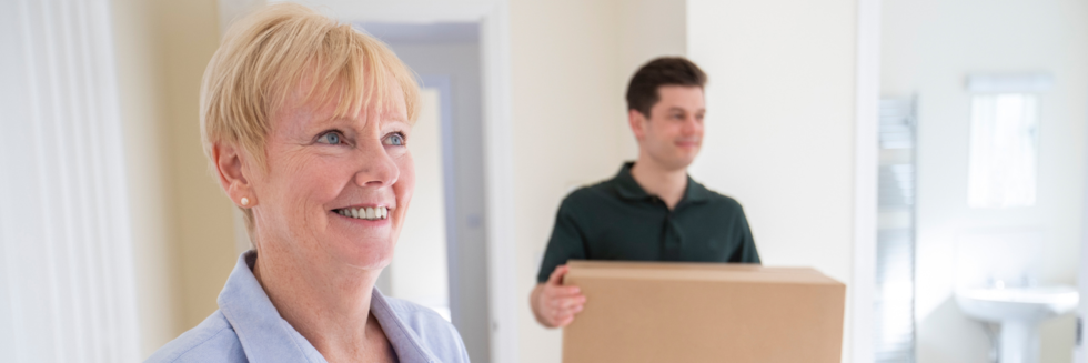 Two people inside a house and the male holds a cardboard box