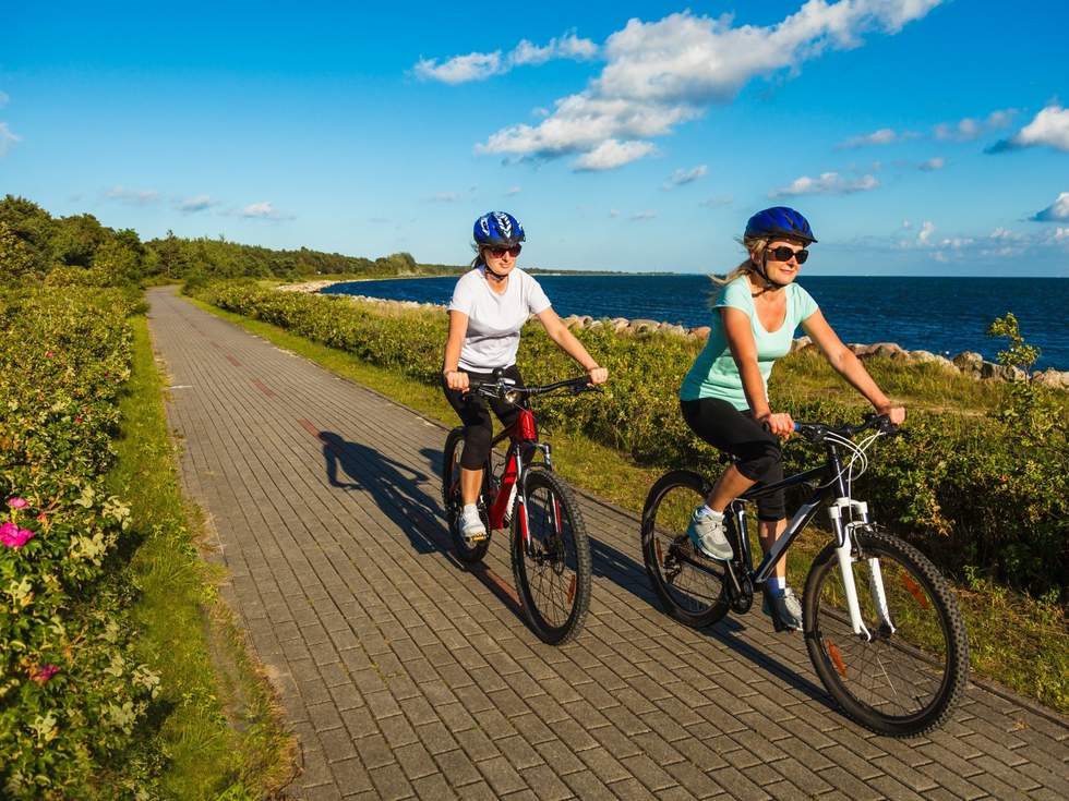 Two women riding bicycles next to the beach