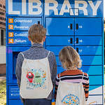 Two children wearing library backpacks standing in front of library lockers