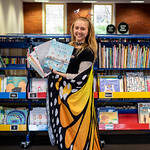 A young staff member dressed in butterfly wings holding two children's books smiling