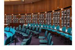 Rows of aqua chairs in Council Chambers with black and white portrait photographs on the walls