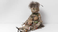 A woven sculpture of two figures made from natural fibres. The larger figure holds the smaller figure in her lap.
