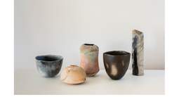 Five ceramic vessels of different size, form and colour placed side by side on a white surface.