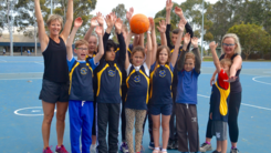 Coaches and boys and girls netball team standing with hands raised in the air