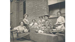 Black and white photo of early 20th century women seated outside having tea and lunch.