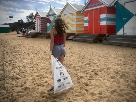 Person with rubbish bag collecting litter from beach outside bathing boxes 