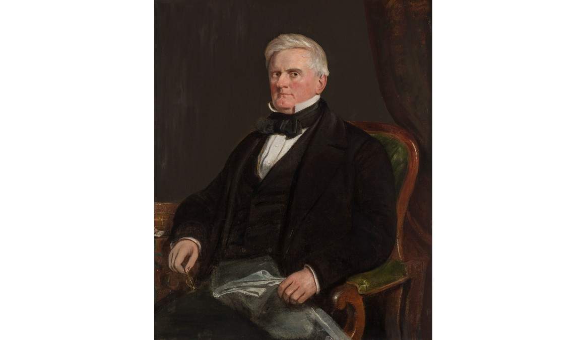 Painting of a gentleman with white hair seated in a green armchair. He holds a newspaper in his hands and wears a black suit.