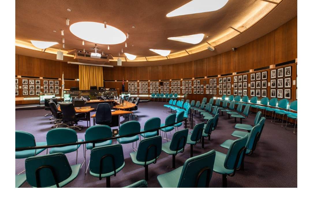 Interior Council Chambers with aqua chairs around small tables and chairs and portraits on the walls