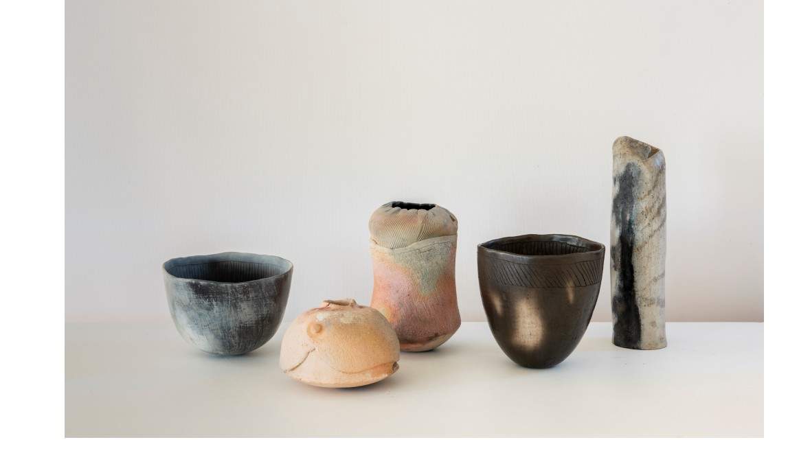 Five ceramic vessels of different size, form and colour placed side by side on a white surface.