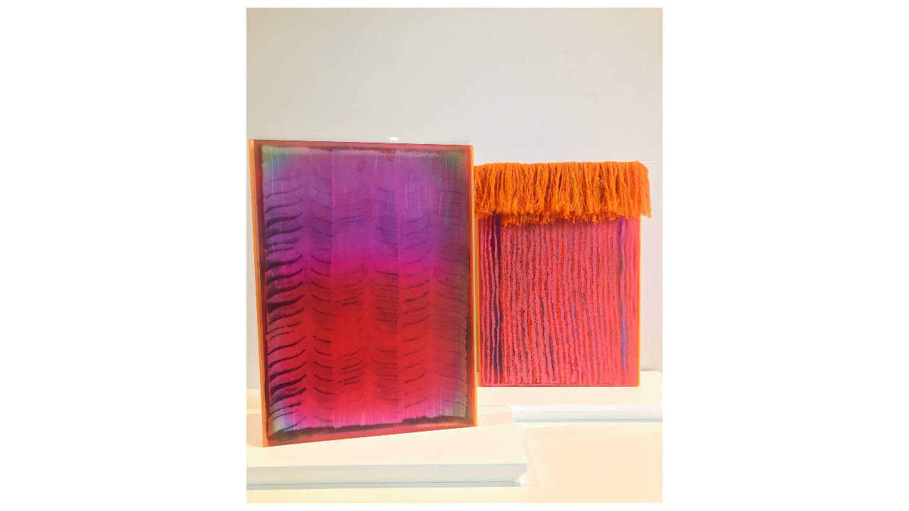 Two artworks painted in purple, pink and orange stand side by side on a white base, one with an orange fringe of nylon threads.