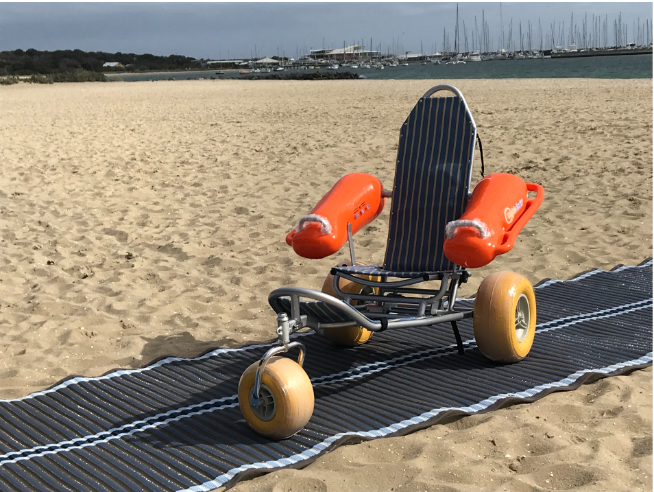 Mobi chair beach wheelchair and access matting on sand with beach and boats in background