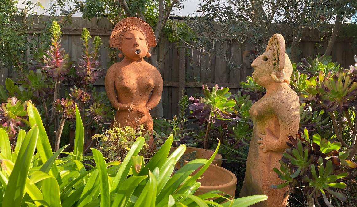 Two terracotta sculptures of women in a garden.