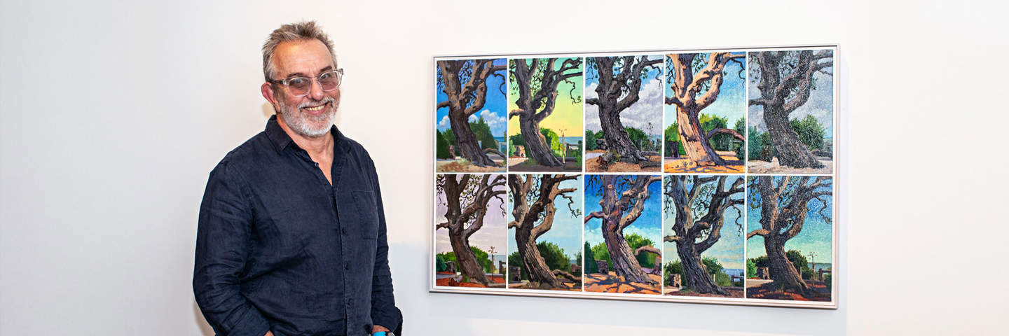 Gregory Alexander stands beside his painting of a series of trees.
