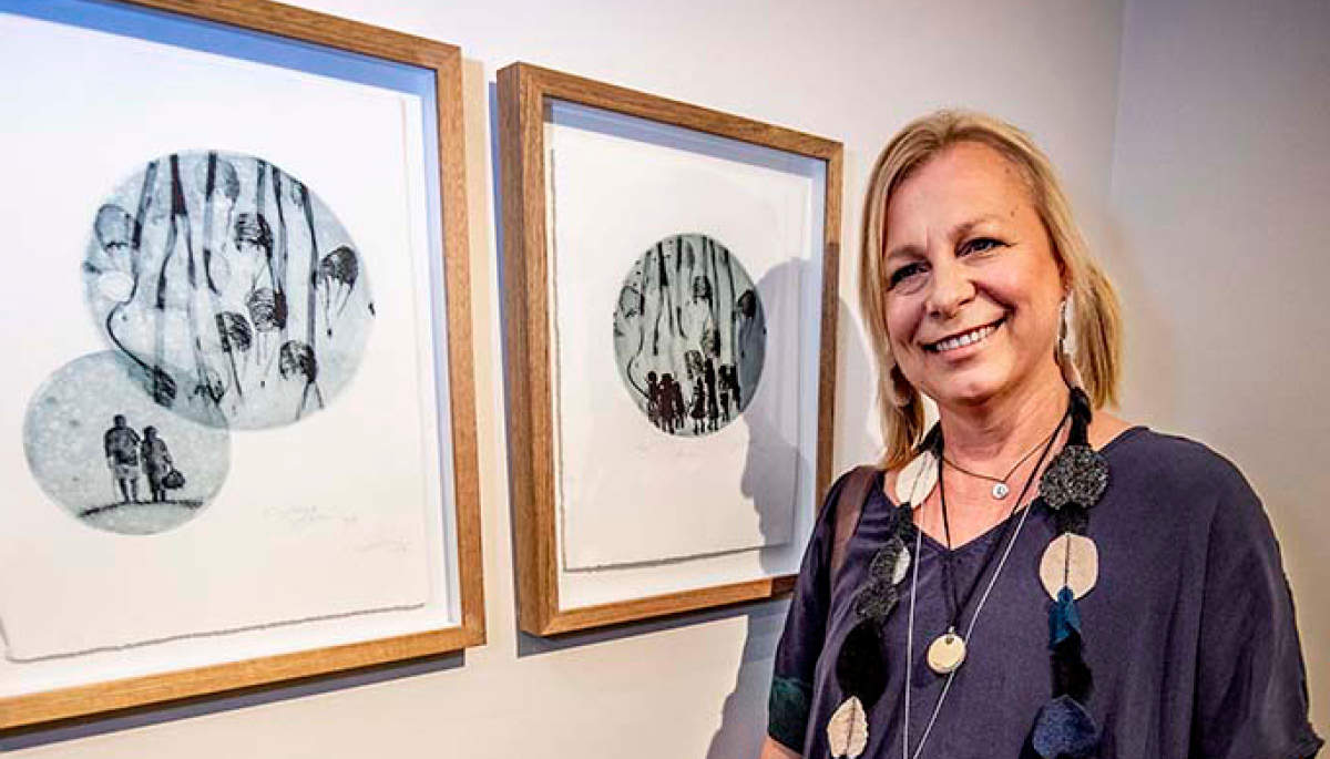Lisa Sewards stands beside her two framed etchings at Bayside Gallery 