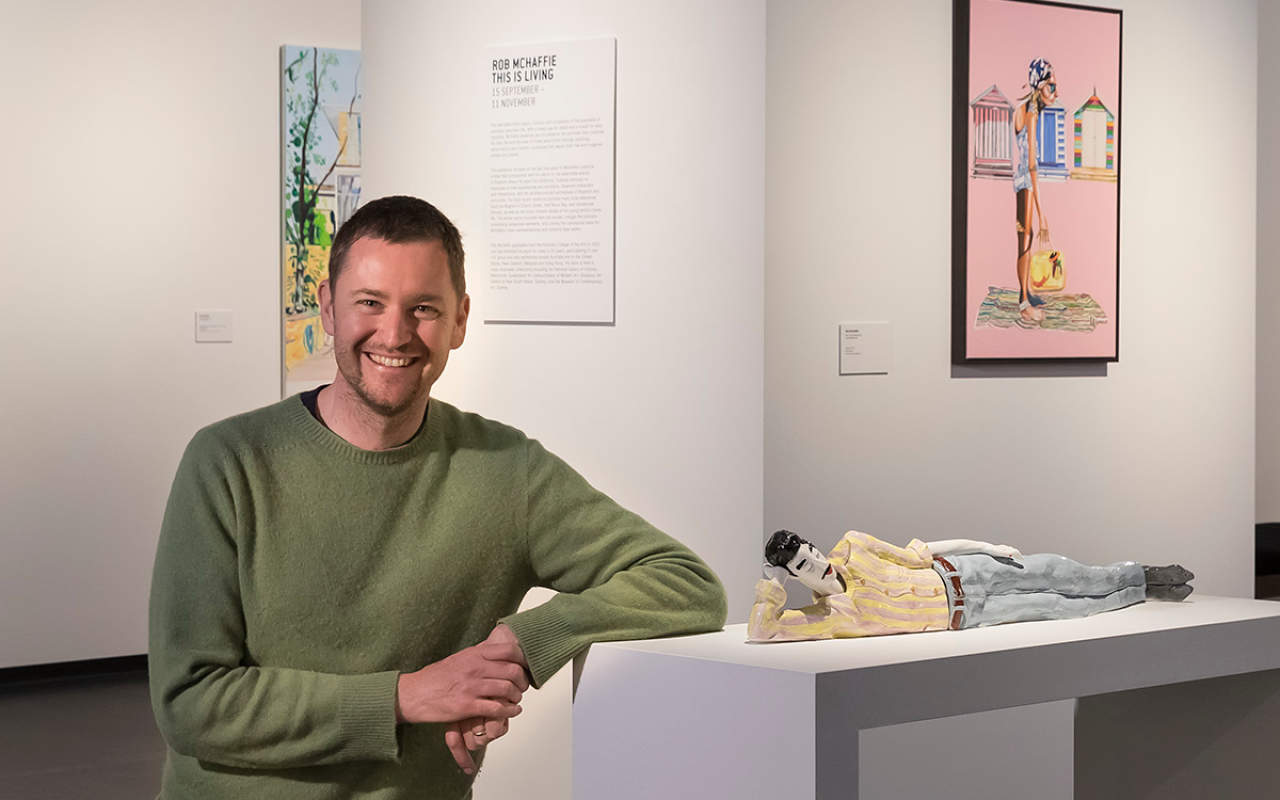 Rob McHaffie standing in an art gallery next to a ceramic reclining figure of a man.