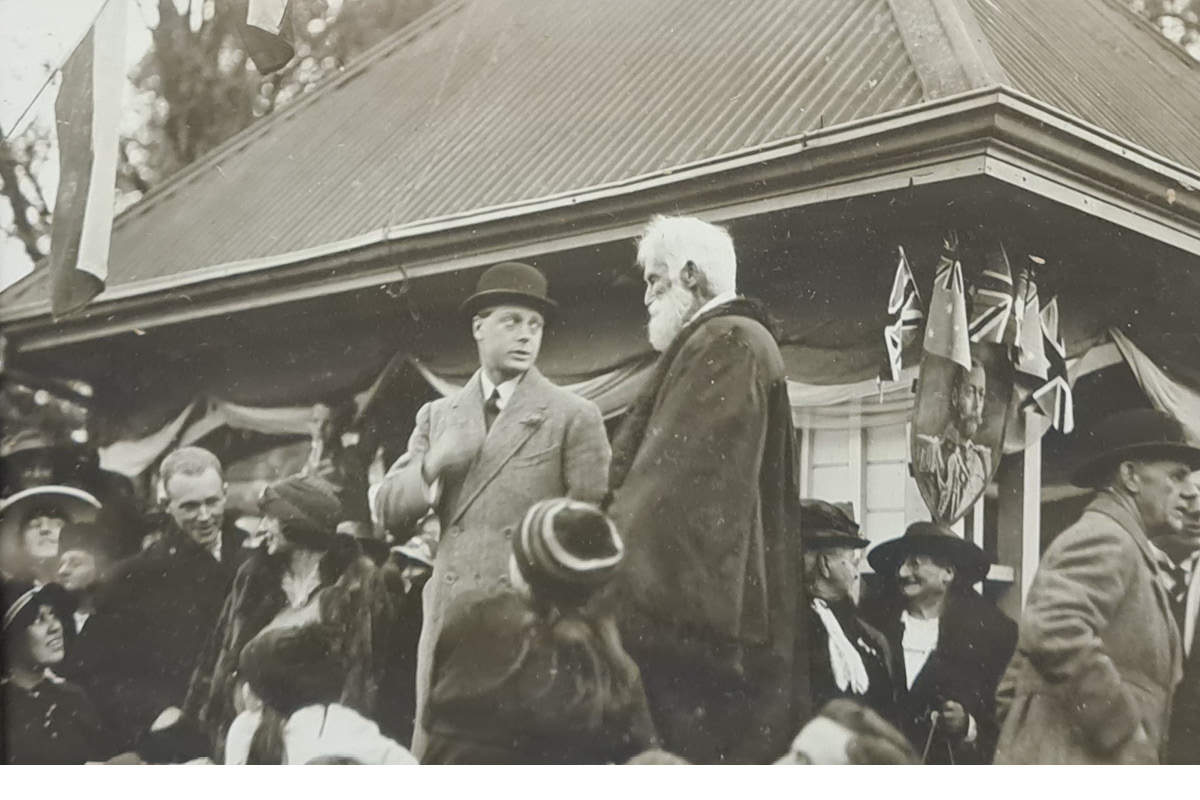 Black and white photograph of two men, one in a bowler hat, one with a grey beard, surrounded by people.