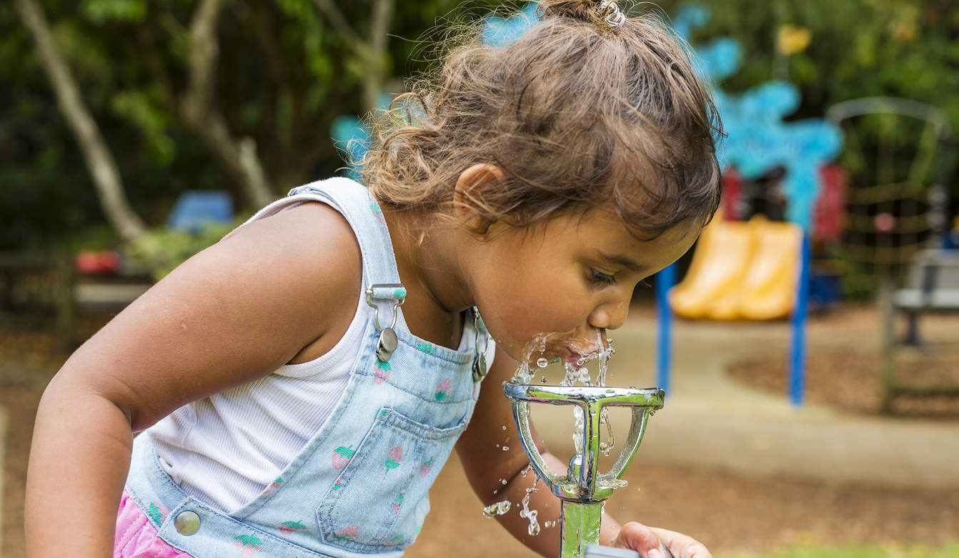 Young girl drinks from water fountain