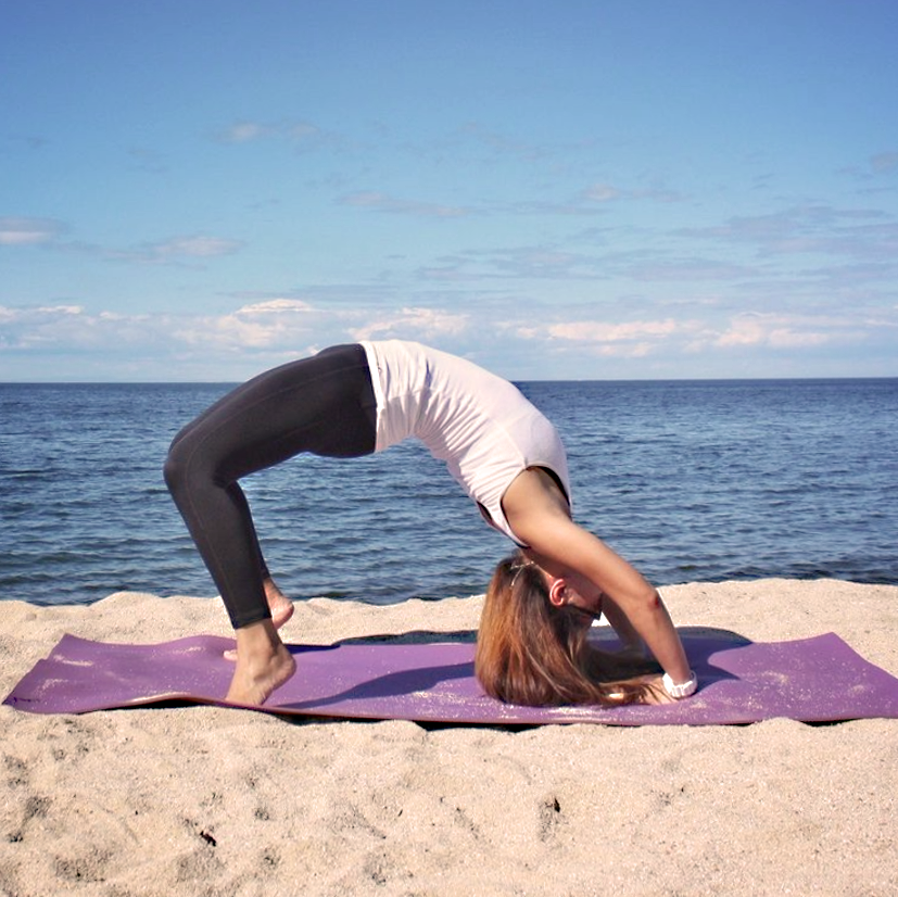 Young person on beach doing a backbend yoga move on a purple yoga mat