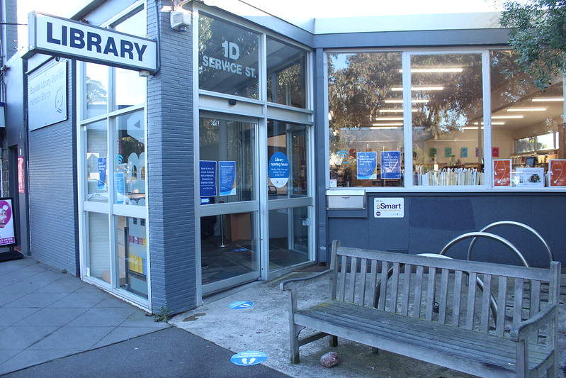 Exterior shot of small blue library with wooden bench out front
