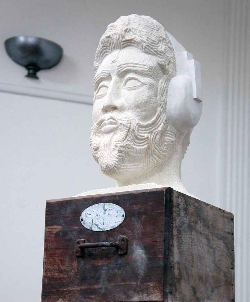 A sculptured sandstone head of a bearded man wearing headphones.
