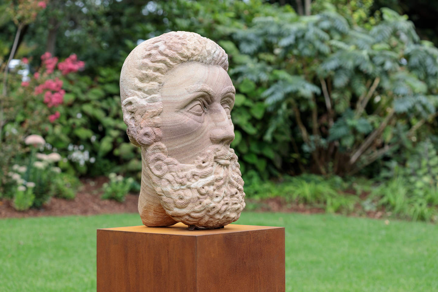 A sandstone sculptured head of a bearded man on a plinth in Billilla gardens. 