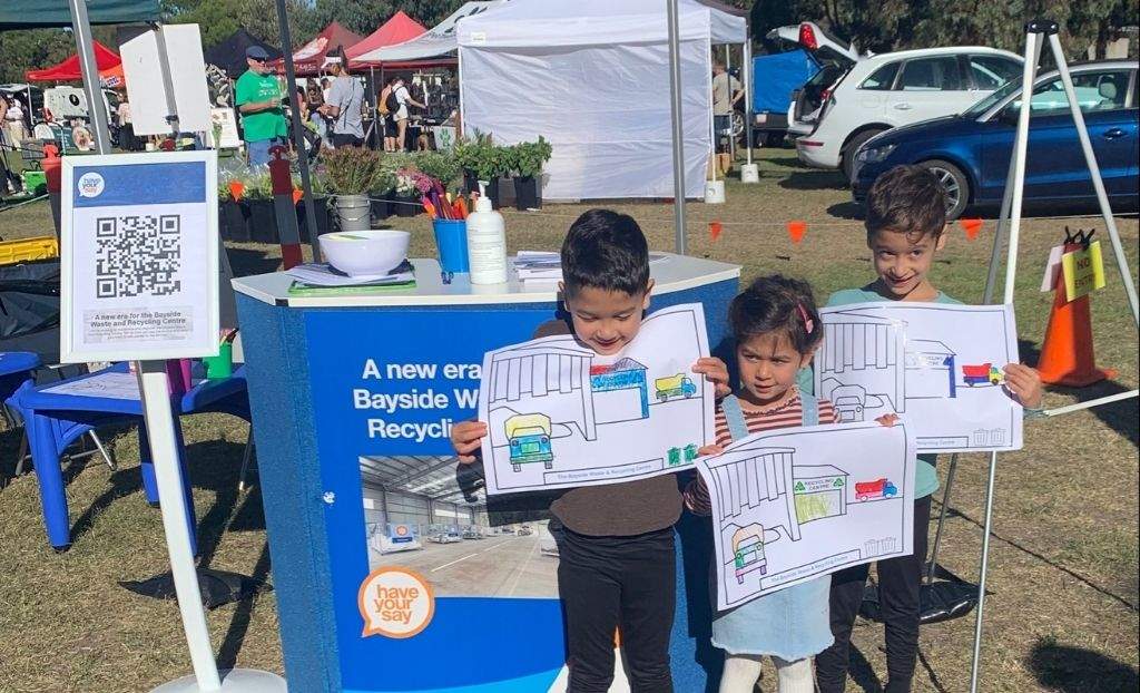 Three cute children with colouring in pages outside Have Your Say tent